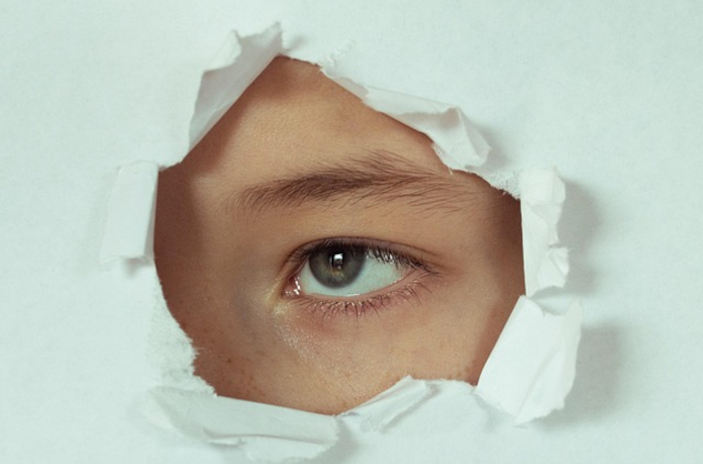 A person looking through a punched-out hole in a sheet of paper. Image by Victoria from Pixabay.&nbsp;