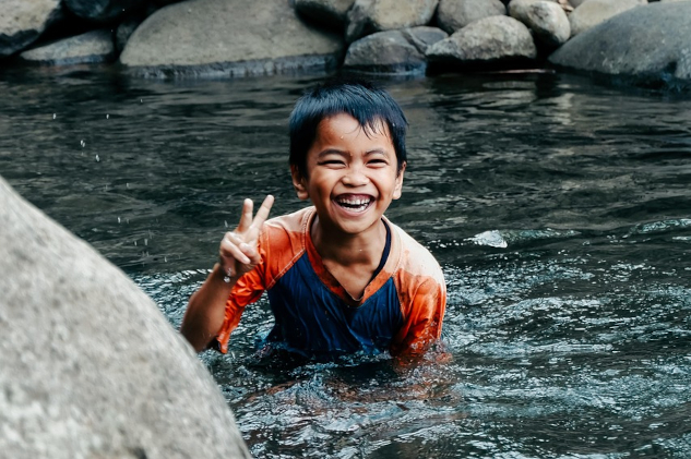 A boardly smiling young boy in a pool of gurgling water. Image by Rona Abdullah from Pixabay.