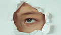 A person looking through a punched-out hole in a sheet of paper. Image by Victoria from Pixabay.&nbsp;